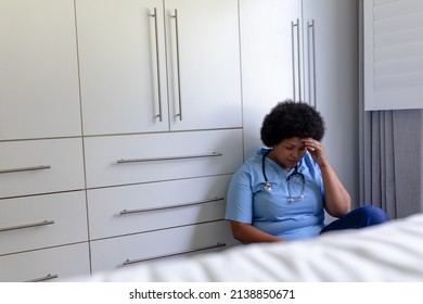 African American Mid Adult Female Nurse With Head In Hand Sitting On Floor In Hospital. Unaltered, Healthcare Worker, Stress, Expertise And Occupation Concept.