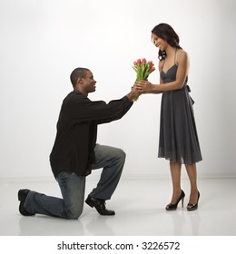 African American mid adult man on knees giving woman bouquet of flowers.