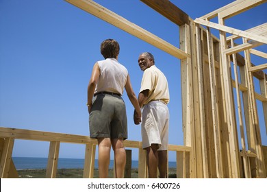 African American middle aged couple holding hands in new home construction at beach.