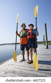 African American Middle-aged Couple Standing On Boat Dock Holding Paddles And Smiling At Viewer.