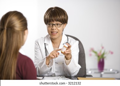 African American Middle-aged Female Doctor Sitting At Desk Explaining Medication To Caucasian Mid-adult Female Patient.