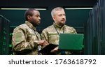 African american military man in camouflage tapping on tablet computer and talking with Caucasian colleague with laptop computer. Server analytic center. Discussion of mixed-races army workers.