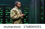 African American military man in uniform and headset working in servers room, tapping on tablet device and speaking in mic. Work with secret information in army. Digital data defence concept.