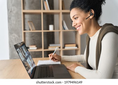 African American mixed race adult student wearing headset having virtual meeting online call educational webinar chatting at home office writing notes. Video e learning conference call on pc.