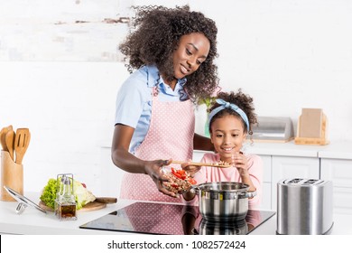 african american mom and daughter cooking on electric stove together