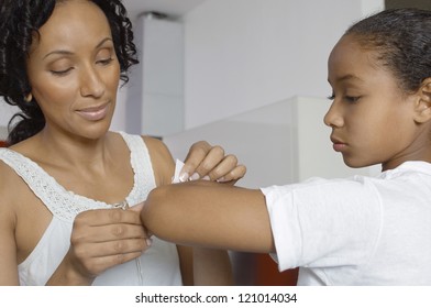 African American Mother Applying Band Aid To Daughter