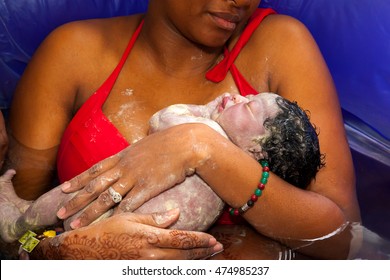 An African American mother cradles her newborn daughter after giving birth at home in a birthing pool of water.
