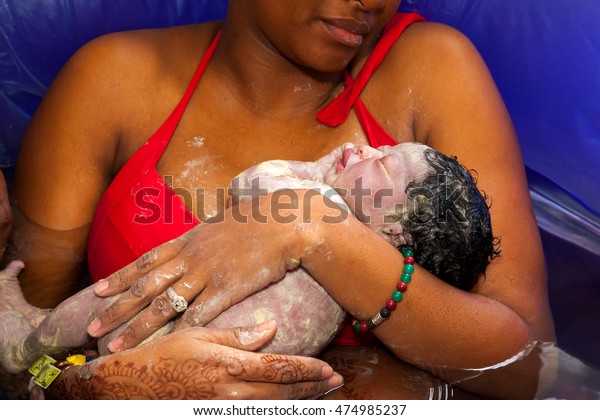 An African\
American mother cradles her newborn daughter after giving birth at\
home in a birthing pool of\
water.