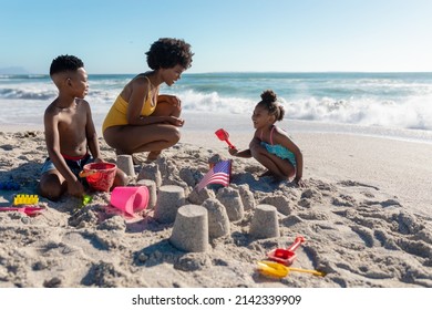 African american mother crouching by children making sandcastles at beach on sunny day. unaltered, family, lifestyle, togetherness, enjoyment and holiday concept. - Powered by Shutterstock