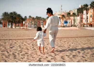 African American mother with cute baby son in white clothes running and playing on the sandy beach by the sea at sunrise. - Powered by Shutterstock