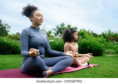 African american Mother daughter doing yoga exercises on grass in park at day time. People having fun outdoors. Concept of friendly family and of summer vacation. Mom and child in the lotus position. - Powered by Shutterstock