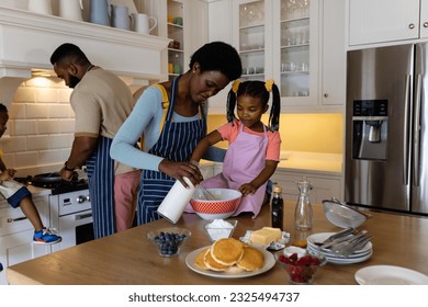 African american mother and daughter mixing batter in bowl while father and son making pancakes. Unaltered, lifestyle, family, love, togetherness, childhood, food, preparation and kitchen concept. - Powered by Shutterstock