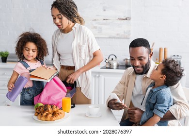 african american mother and daughter packing backpack together in kitchen - Powered by Shutterstock