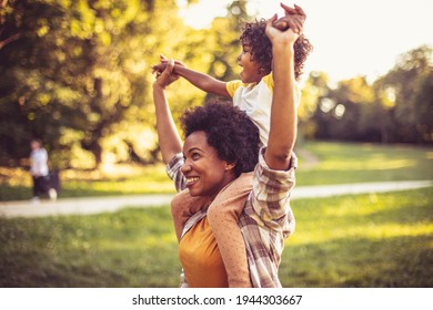 African American mother and daughter playing in the park. Mother carrying daughter on shoulders. 