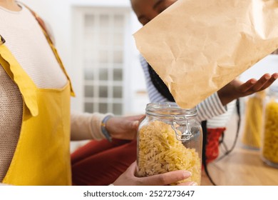 African american mother and daughter pouring pasta to glass jar in kitchen at home, copy space. Expression, togetherness, motherhood, childhood, food and drink and domestic life, - Powered by Shutterstock