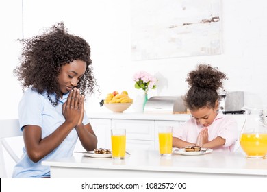 african american mother and daughter praying before breakfast in kitchen - Powered by Shutterstock