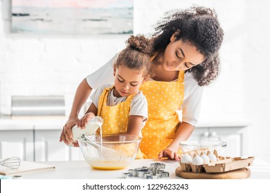 African American Mother And Daughter Preparing Dough And Pouring Milk Into Bowl In Kitchen