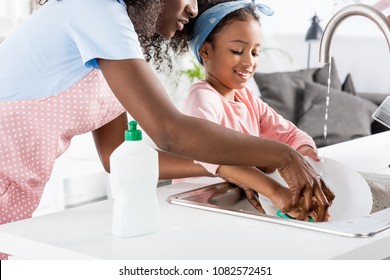 african american mother and daughter washing dishes with detergent on kitchen - Shutterstock ID 1082572451