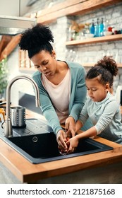 African American Mother And Daughter Washing Vegetables Together Under The Kitchen Sink.