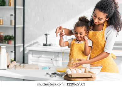 african american mother and daughter whisking eggs for dough in kitchen - Powered by Shutterstock