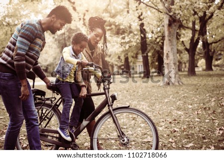  African American mother and father teaching their daughter to drive bike in park.