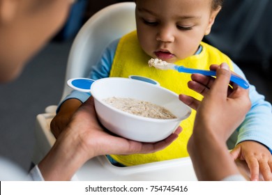 african american mother feeding little son with porridge at home