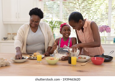 African american mother and grandmother teaching girl cooking in the kitchen. three generation family spending time together.