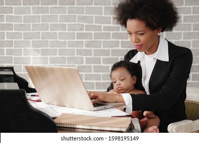 African American Mother Holding Her Baby Boy On Hands While Working With Laptop Computer At Home