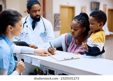 African American mother holding her small son while filling medical paperwork at reception desk in the hospital. - Powered by Shutterstock