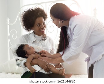 African American mother holding sick mix race child while Asian doctor checking up and talking happily with baby boy.