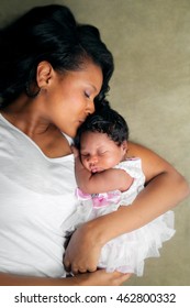 An African American Mother Lays On Her Side, Holding Her Newborn Daughter.  She Kisses Her On The Top Of Her Head.