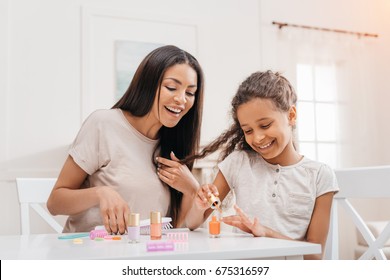 african american mother looking at happy daughter doing manicure at home - Powered by Shutterstock