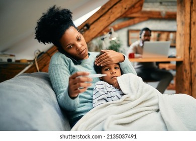 African American Mother Measuring Sick Son's Temperature While Talking To The Doctor Over The Phone.