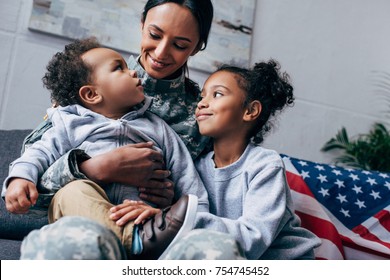 african american mother in military uniform sitting with her children, american flag on background - Powered by Shutterstock