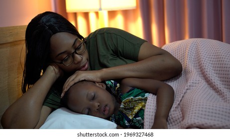 African American Mother Singing Lullaby For Little Daughter Before Going To Sleep On Bed At Home. Black Mom Story Telling To Girl In Bedroom. Sleeping Child In Parent Embrace . Kid Hug Teddy Bear 