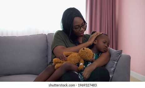 African American Mother Singing Lullaby For Little Daughter Going To Sleep On Sofa In Living Room . Black Mom Story Telling To Girl On Couch . Sleeping Child In Parent Embrace . Kid Hug Teddy Bear 