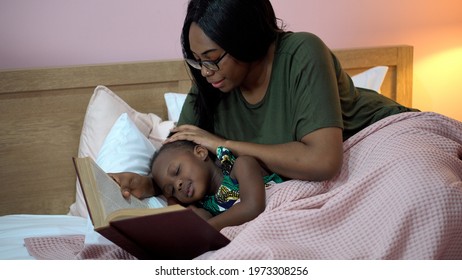 African American Mother Singing Lullaby For Little Daughter Before Going To Sleep On Bed At Home. Black Mom Story Telling To Girl In Bedroom. Sleeping Child In Parent Embrace . Kid Hug Teddy Bear 