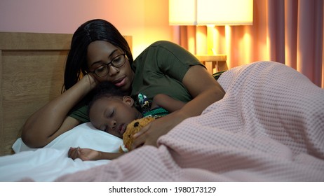 African American Mother Singing Lullaby For Little Daughter Before Going To Sleep On Bed At Home. Black Mom Story Telling To Girl In Bedroom. Sleeping Child In Parent Embrace . Kid Hug Teddy Bear 