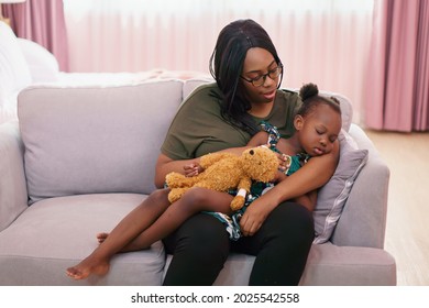 African American Mother Singing Lullaby For Little Daughter Going To Sleep On Sofa In Living Room . Black Mom Story Telling To Girl On Couch . Sleeping Child In Parent Embrace . Kid Hug Teddy Bear 