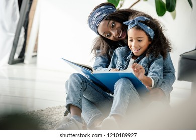 African American Mother And Smiling Daughter Looking At Family Photo Album At Home