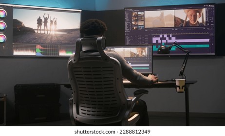 African American multimedia artist drinks coffee and makes color grading in editing program on computer. Process of video post production in modern studio. Multiple monitors with travel movie footage. - Shutterstock ID 2288812349