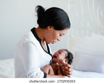 African American Mum Is Comforting A Baby On A White Bedroom