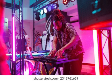 African american musician performing live on stage with spotlights at club using mixer console. Man dj pressing buttons on controller while mixing sound at nightclub disco party - Powered by Shutterstock