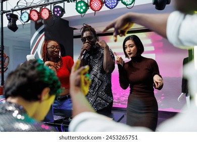 African american musician singing in microphone at electronic music festival live concert in nightclub. Diverse man and women partying and performing on stage at event in club - Powered by Shutterstock