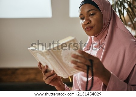 African American Muslim woman reading from Koran while praying at home.