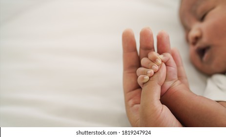 african american new born baby hand holding mom finger on white bed