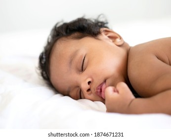 The African American newborn is sleeping soundly on a white mattress.