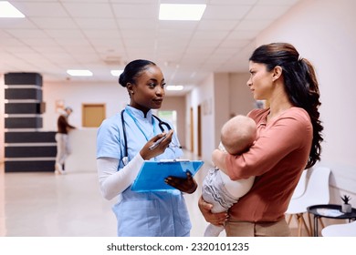 African American nurse communicating with mother who is holding baby daughter in her arms at medical clinic. - Powered by Shutterstock