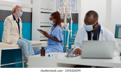 African American Nurse Consulting Senior Patient Using Tablet To Take Notes, Doing Examination During Covid 19 Pandemic. Specialist And Elderly Woman Having Checkup Visit Appointment.