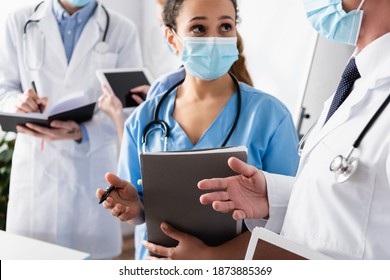 African American Nurse In Medical Mask Talking To Doctor With Blurred Colleagues On Background